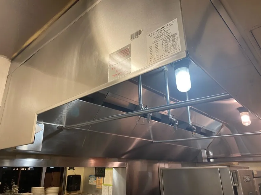 Commercial kitchen hood with a Miguel's Steam Cleaning service label after cleaning