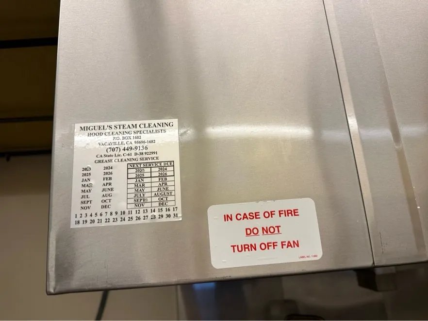 Service label next to an 'In case of fire do not turn off fan' sticker on a hood