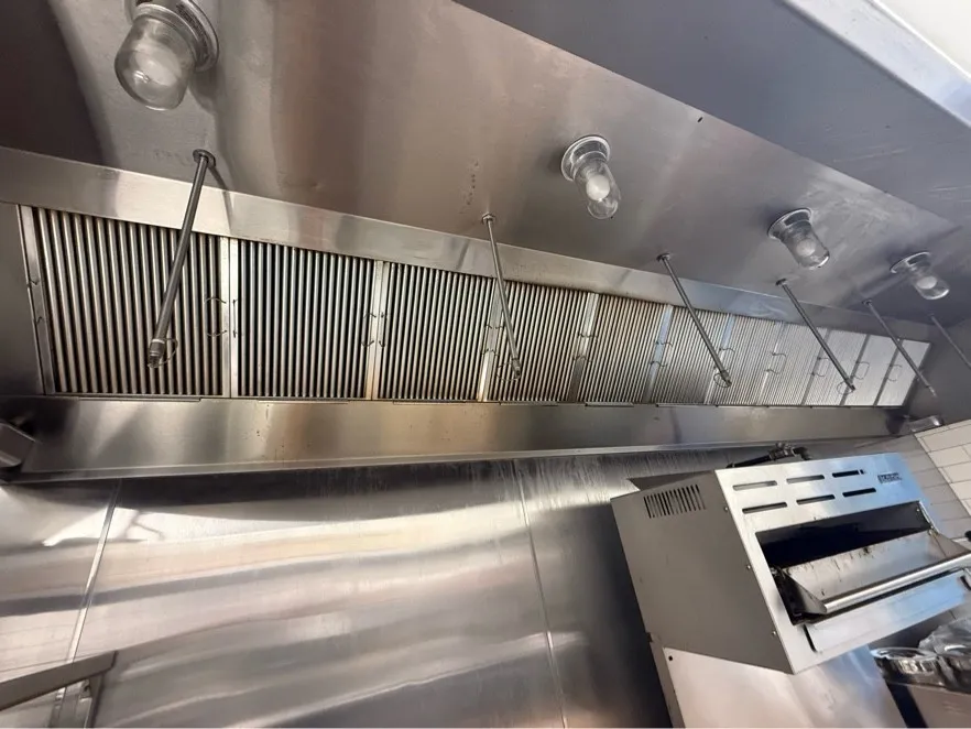 Long stainless restaurant hood with clean baffle filters above a broiler